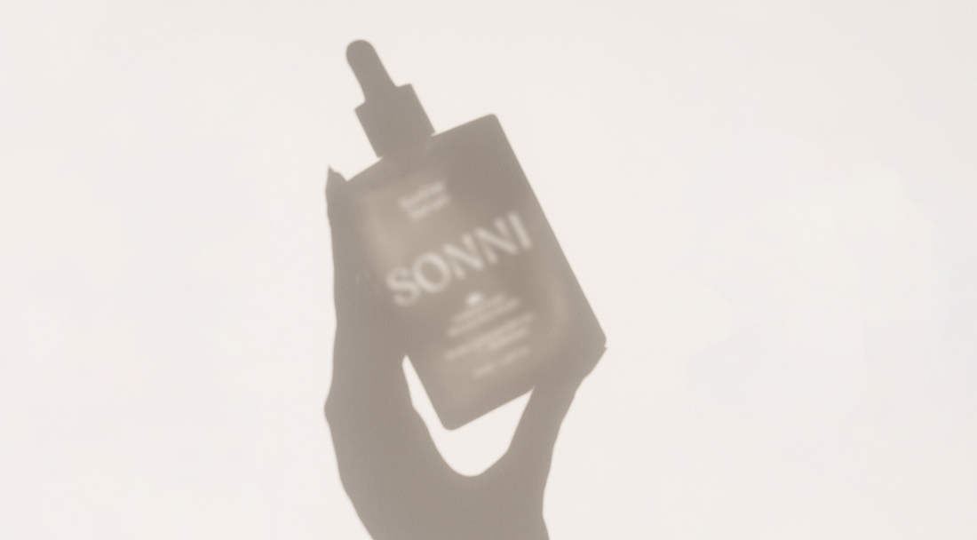 Soft shadow of a hand holding a SONNI SunDay Mineral Serum bottle against a light background.