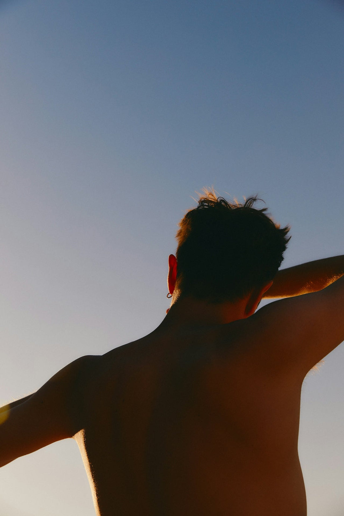 Back view of a man outdoors at sunset, highlighting the importance of daily mineral sunscreen for full-body sun protection.