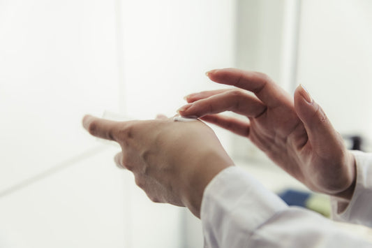 Hands rubbing a small amount of white cream into skin