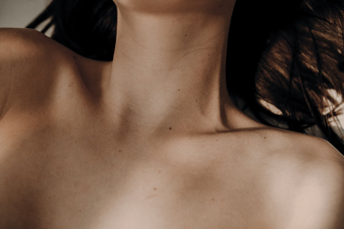 Close-up of a woman’s neck and collarbone in soft natural light, highlighting smooth, bare skin with a few natural freckles and moles visible.
