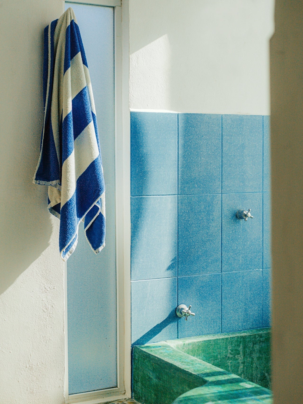 A striped blue and white towel hanging outside a tiled shower with blue and green ceramic tiles.