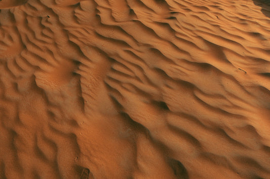 Close-up aerial view of wind-shaped sand dunes creating soft, rippling patterns across warm golden desert sand.