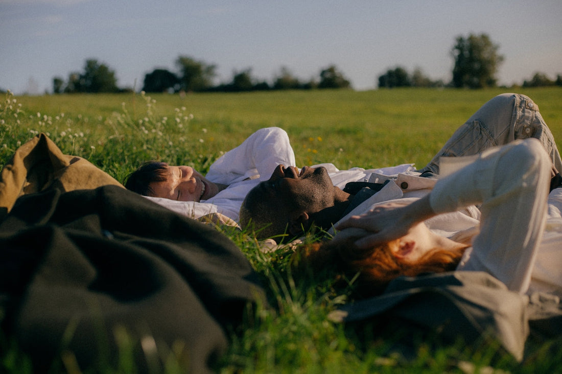 Three people lying on their backs in a sunny green field, eyes closed, relaxing in the afternoon light.