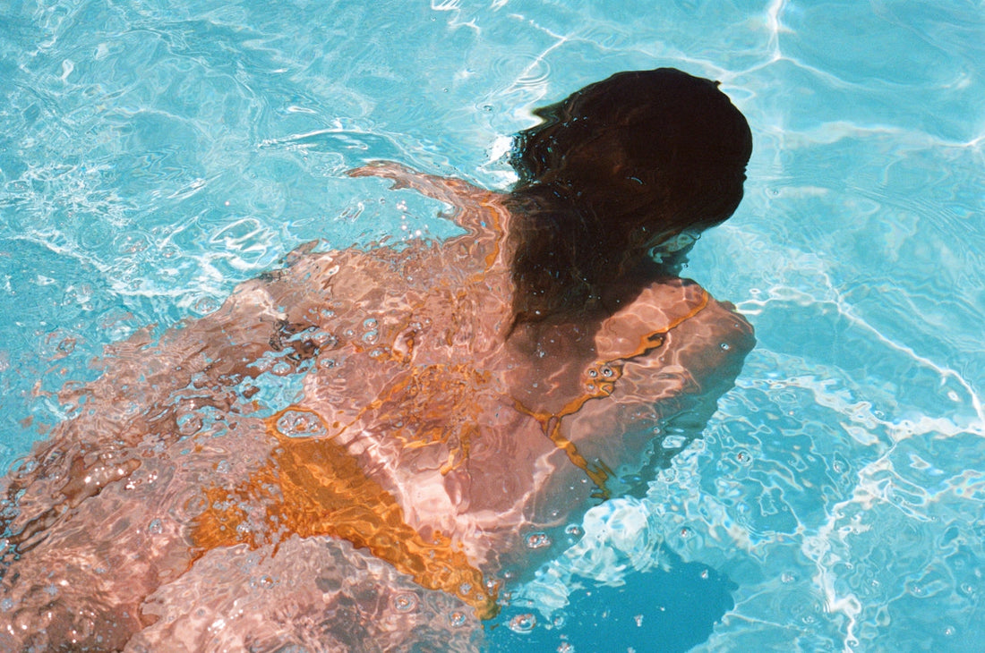 Person swimming underwater in a pool, hair fanned out beneath the surface.