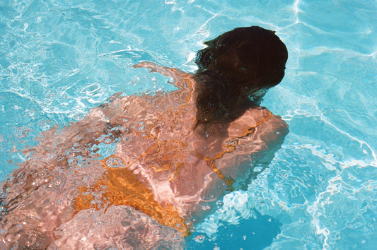 Person swimming underwater in a pool, hair fanned out beneath the surface.