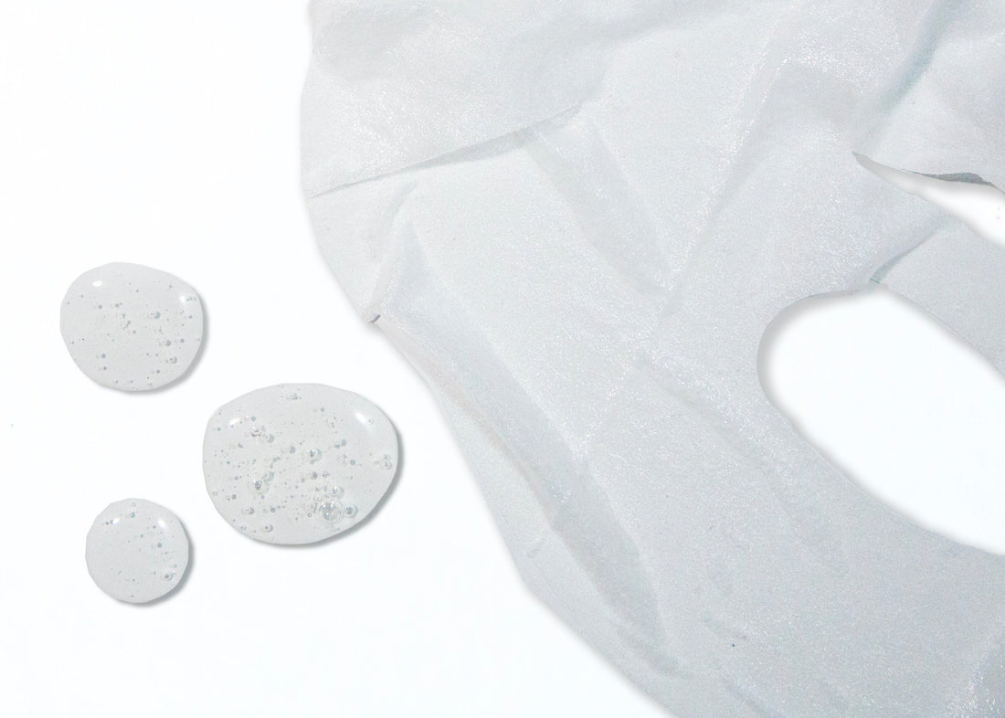 Close-up of a hydrating sheet mask with droplets of serum on a white background.