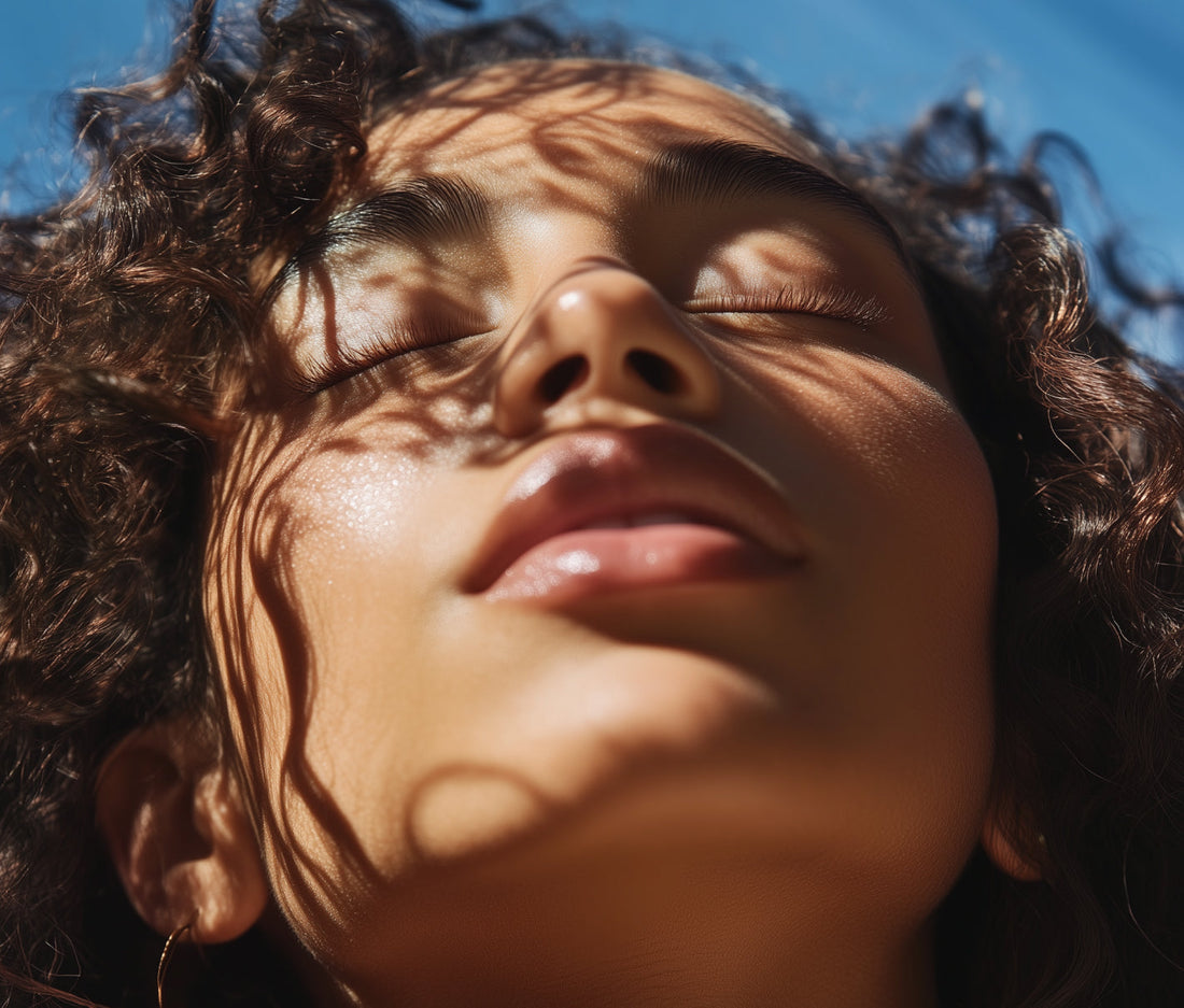 Close-up of a person’s face in sunlight, eyes closed, with soft shadows across the skin and a natural, hydrated glow.